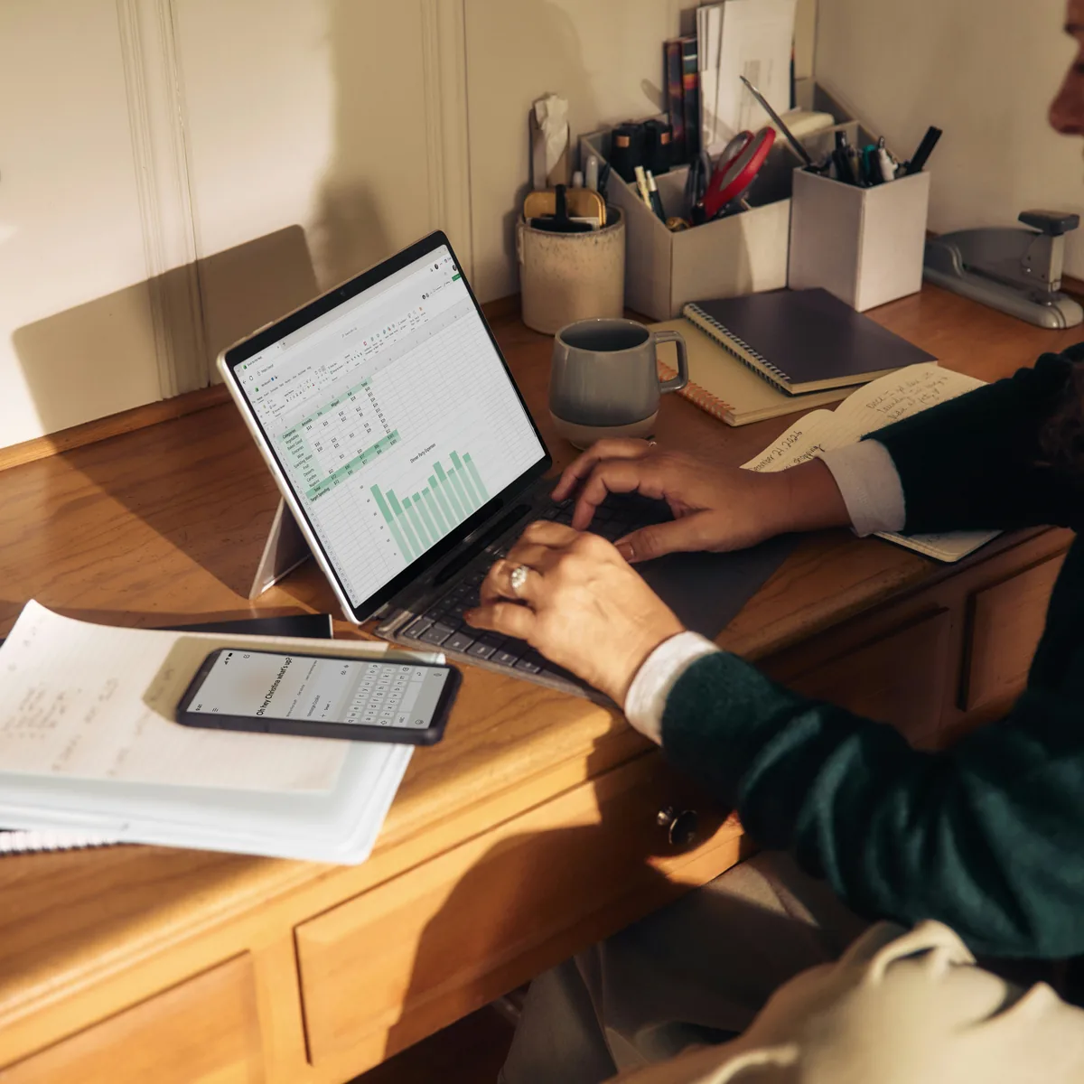 Someone at a sunlit desk working through a spreadsheet on a laptop