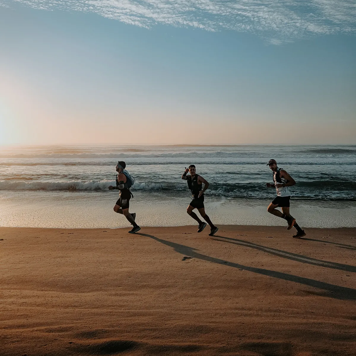 Three people running along the shoreline at sunrise